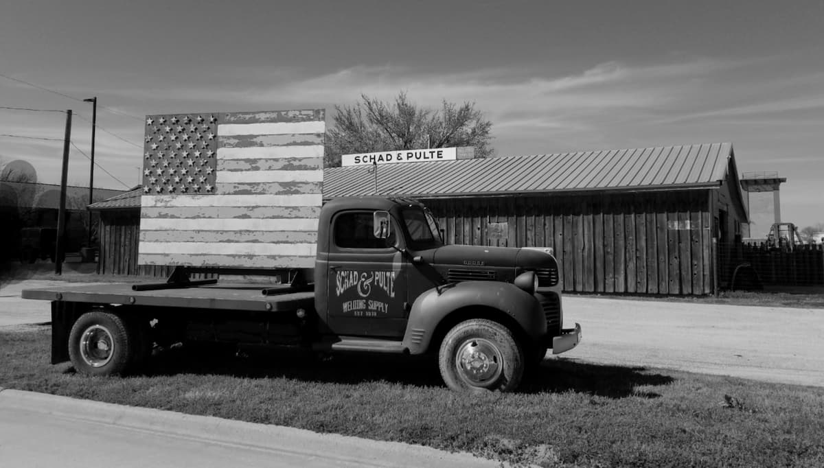 Schad & Pulte's antique flatbed truck carrying a weathered wooden American flag, parked in front of the store in Gainesville, Texas